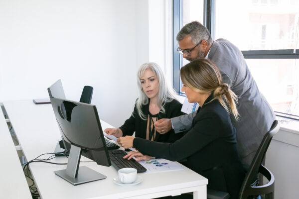 Three business professionals collaborating on a computer in a web design company setting.