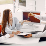 A man and woman display a car key in front of a computer, symbolizing tailored insurance solutions for photographers and contractors.