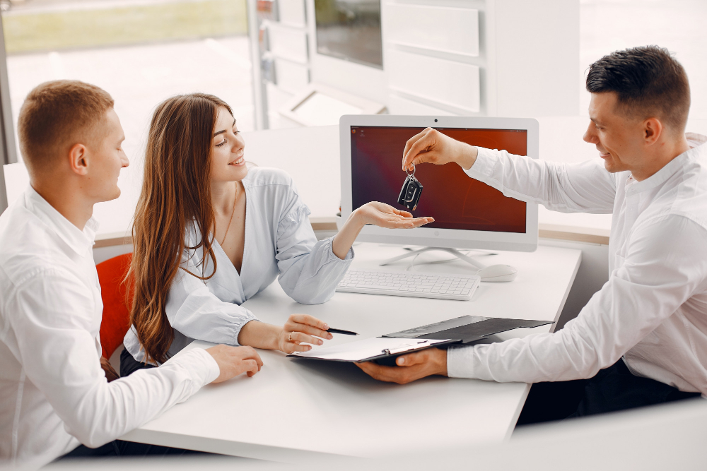 A man and woman display a car key in front of a computer, symbolizing tailored insurance solutions for photographers and contractors.