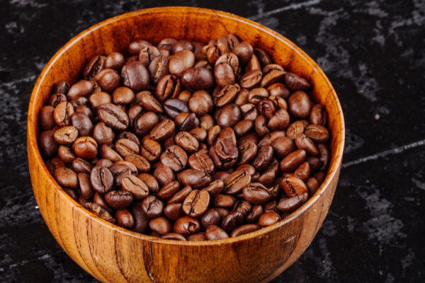 A close-up of medium roast coffee beans in a wooden bowl, elegantly placed on a black surface, showcasing their natural sheen.