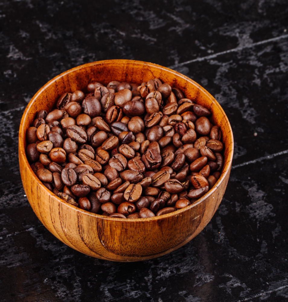 A close-up of medium roast coffee beans in a wooden bowl, elegantly placed on a black surface, showcasing their natural sheen.